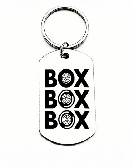 Silver keychain that reads Box Box Box with car tires for the letter O
