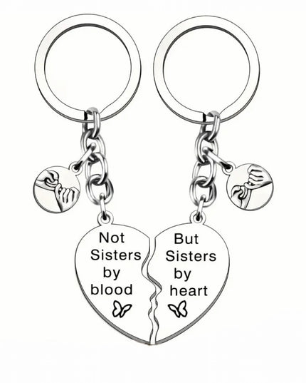 Double keychain and charm set that reads "Not Sisters by blood But Sisters by heart"