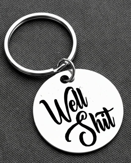 Keychain with 'Well Shit' text on a gray background